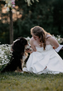 Braut hält die Pfote Ihres Hundes vor dem mit Blumen geschmückten Traubogen.